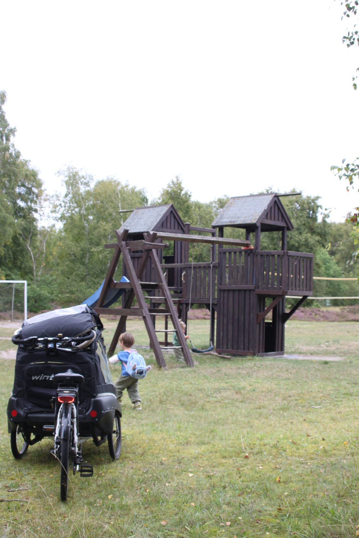 Spielplatz mit Kletterturm und Schaukel am Rand der Heide, Lastenrad im Vordergrund